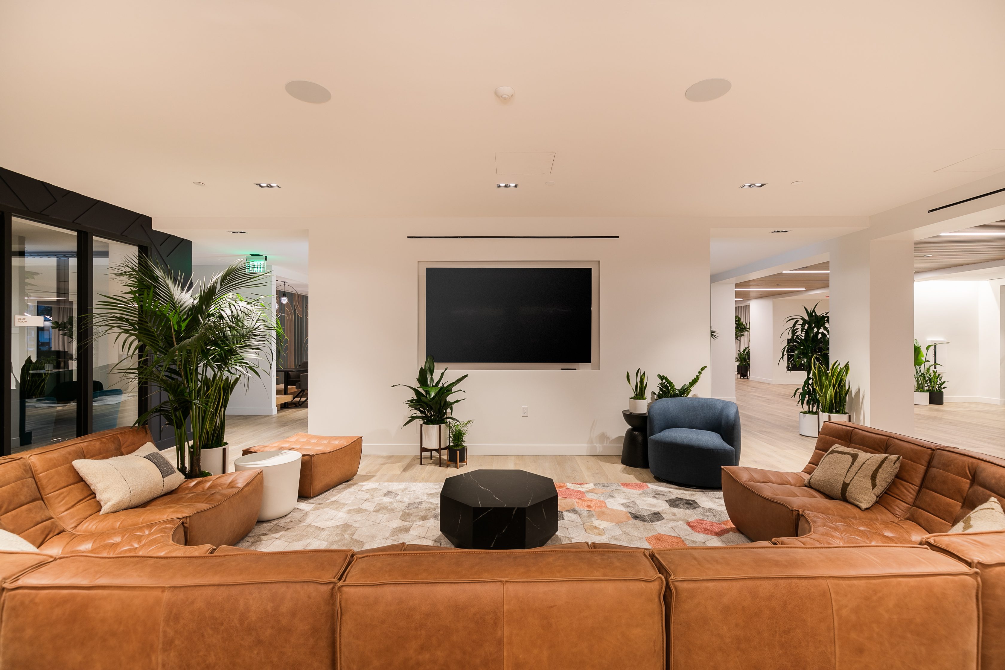 A living room with brown leather furniture and a large tv in The Rinrose multifamily building in Pasadena.