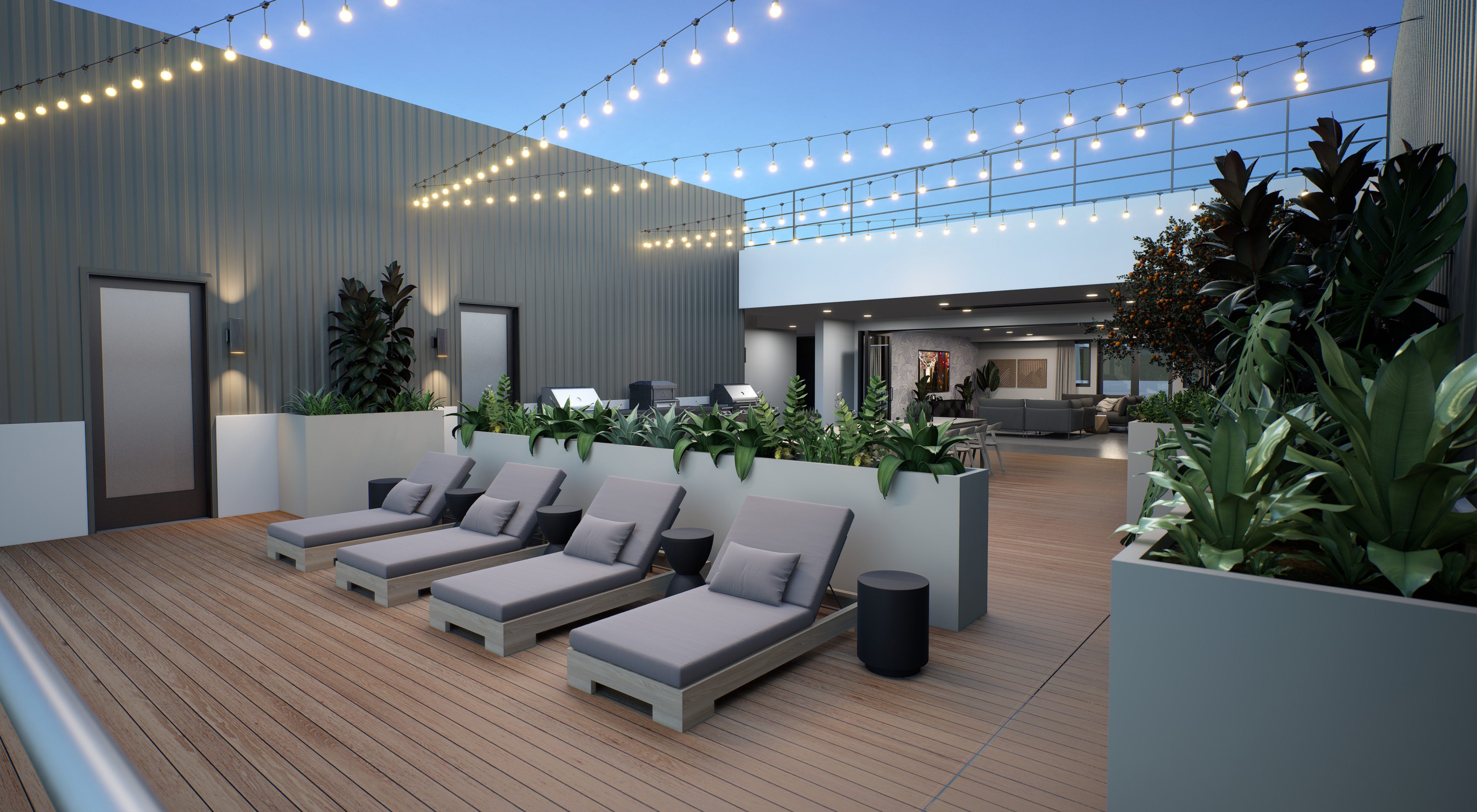 Gray lounge chairs on outdoor patio with greenery and string lights above with outdoor grills behind