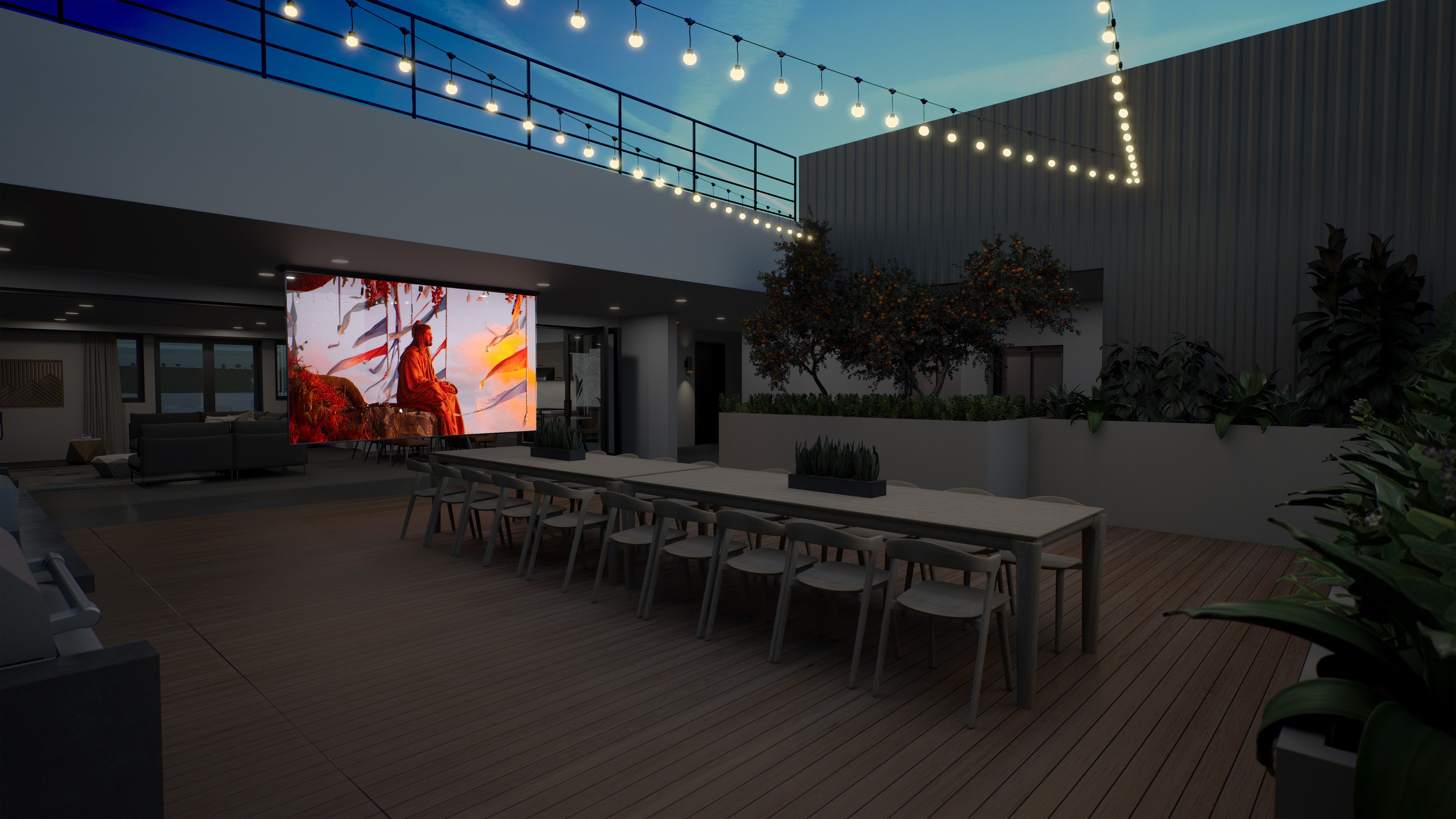 Outdoor patio at night with TV projector screen and long tables with ample seating, greenery surrounding and string lights above