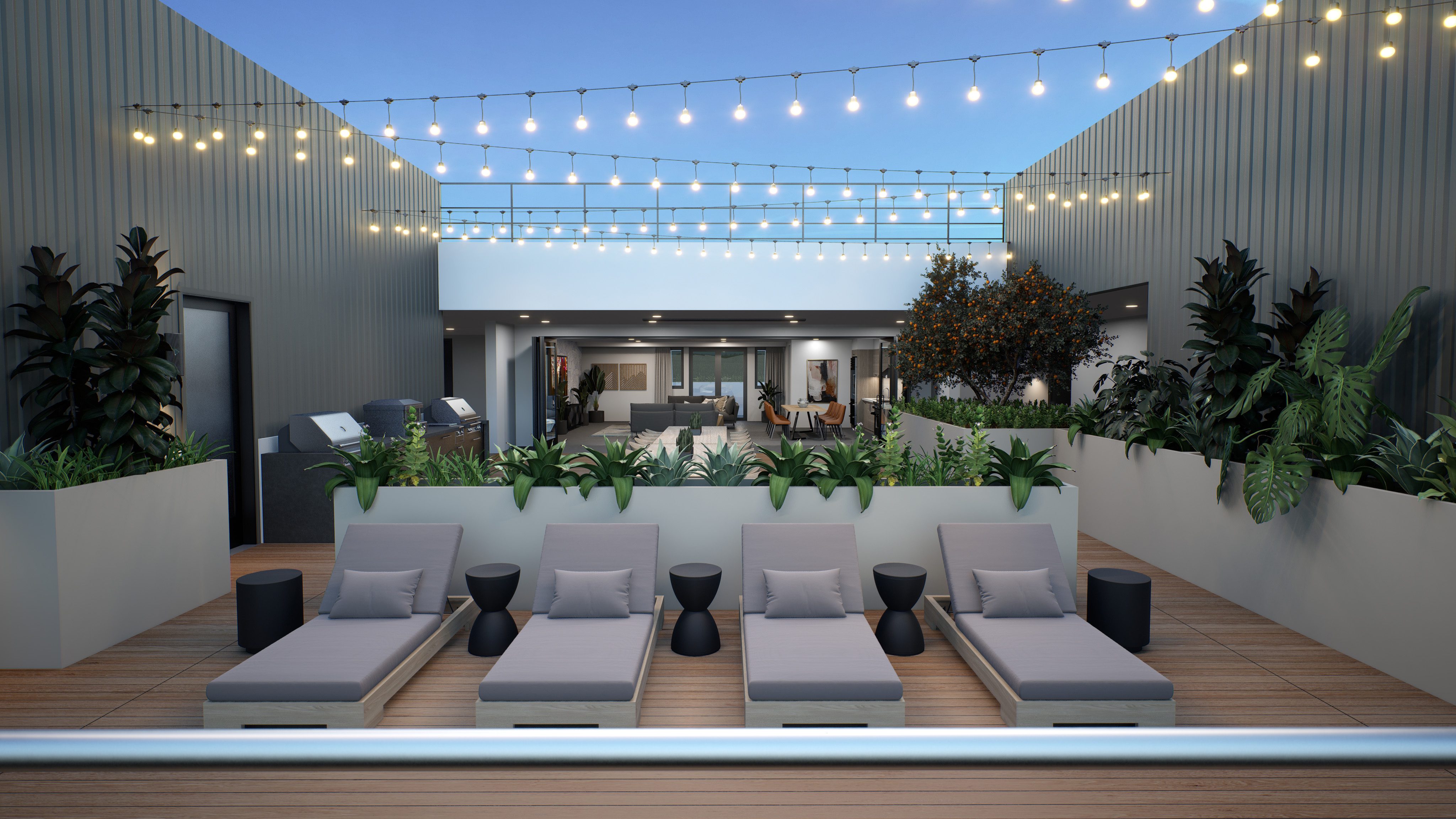 Gray lounge chairs on outdoor patio with greenery and string lights above with open lounge/kitchen area in the background